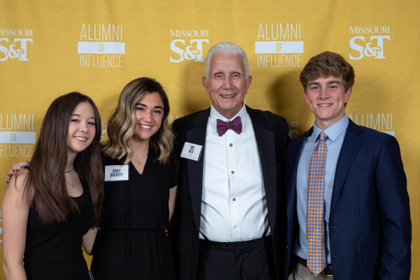 three students pose for a photo with an alumnus